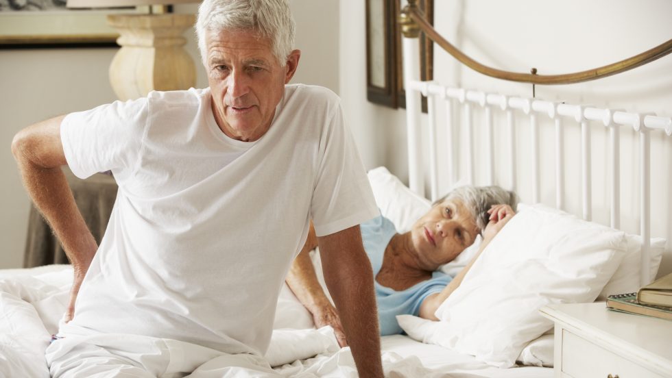 Mann steht mit Schmerzen aus dem Bett auf